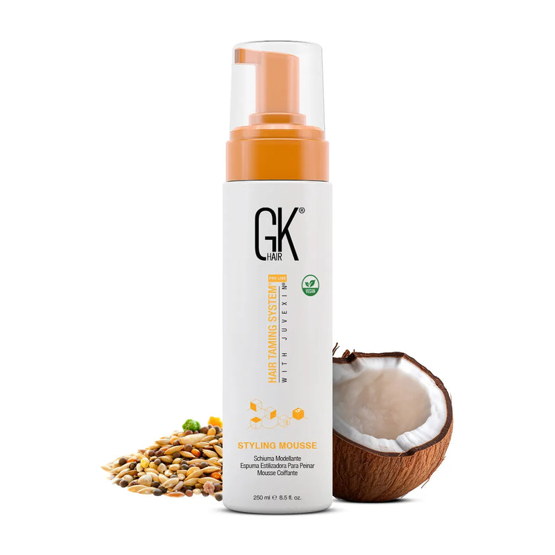 GK Hair Styling Mousse 250 ml white pump bottle with orange collar beside grains and a halved coconut on white