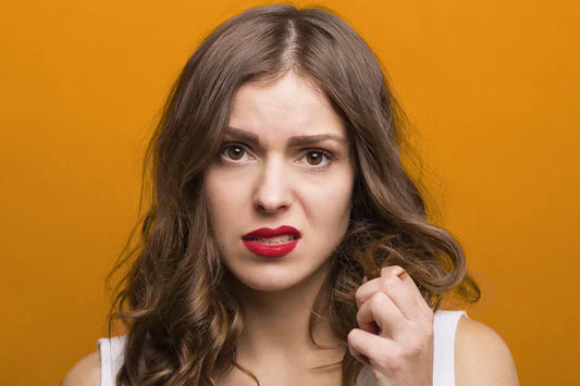 A person with wavy brown hair holding a strand, set against a vibrant orange background.