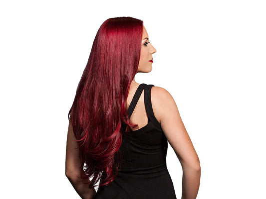 A woman with long, vibrant red hair stands with her back to the camera, wearing a sleek black top.