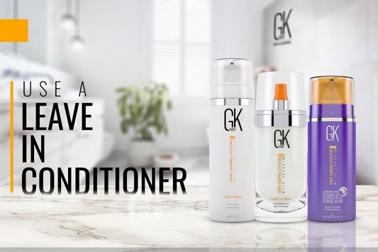 Three GK Hair leave-in conditioner on a marble countertop. Bold text reads 'Use a Leave In Conditioner' against a blurred bathroom background
