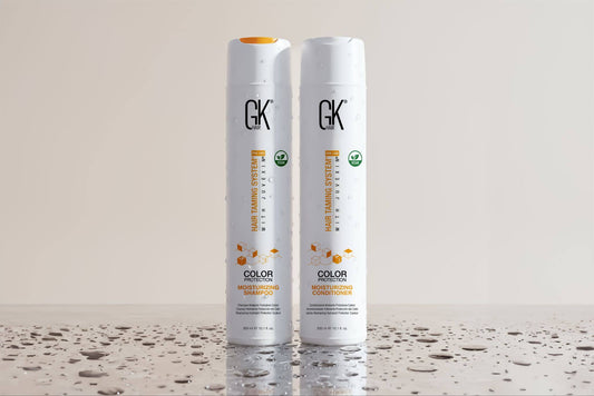 Two bottles of GK hair products, one labeled "Color Moisturizing Shampoo" and the other "Color Moisturizing Conditioner," with droplets on their surfaces.