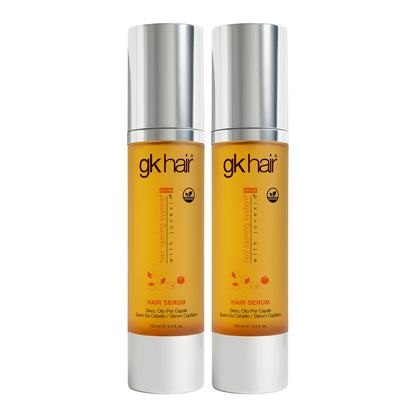 Two 100 ml GK Hair Hair Serum bottles with yellow pumps exposed and their silver caps lying beside them on white